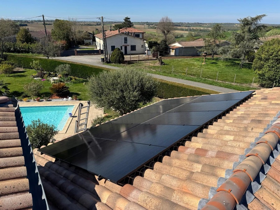 Panneaux solaires noirs posés sur une toiture en tuiles canal, avec vue sur le jardin, la piscine et la campagne